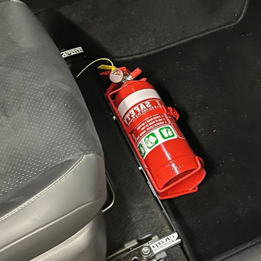Close-up of a red fire extinguisher held in a KAP bracket at the base of the front seat in a Toyota Camry