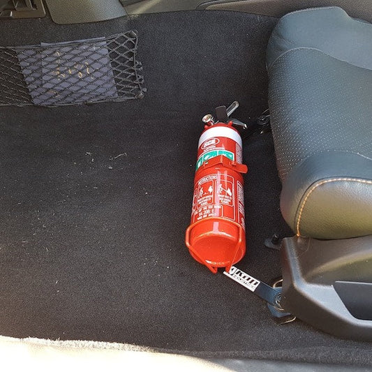 Close-up of a red fire extinguisher held in a KAP bracket at the base of the left front seat in a Nissan 350Z