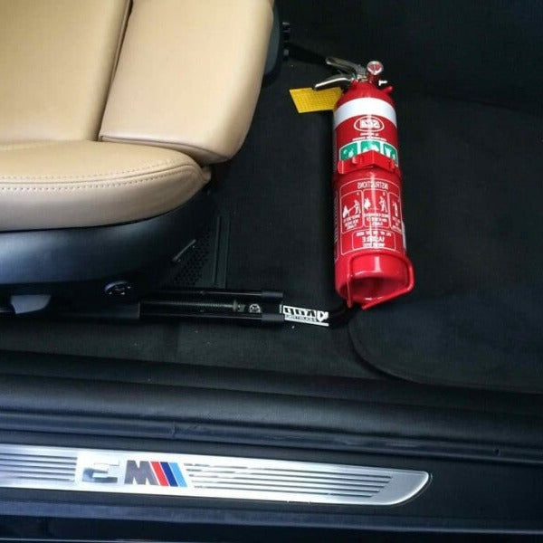 Close-up of a red fire extinguisher held in a KAP bracket at the base of the front seat in a Mini Cooper / JCW