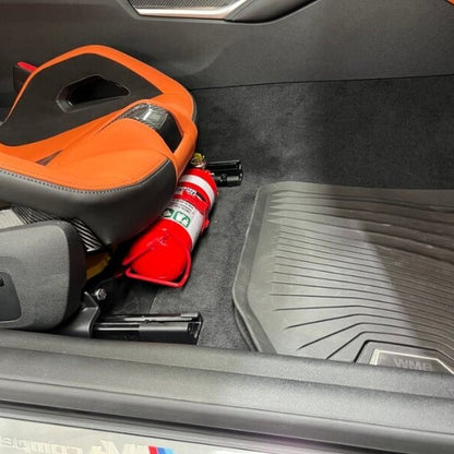 Close-up of a red fire extinguisher held in a KAP bracket at the base of the front seat in a BMW X3 M
