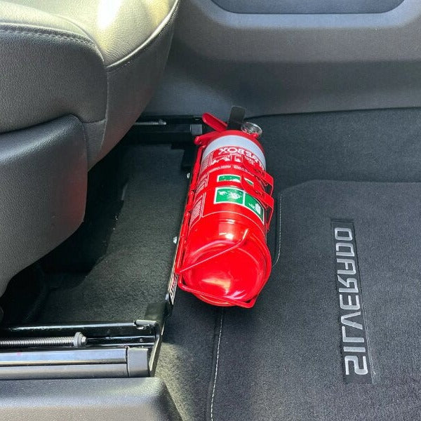 Close-up of a red fire extinguisher held in a KAP bracket at the base of the front seat in a GMC Sierra 1500