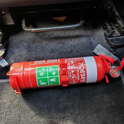 Close-up of a red fire extinguisher held in a KAP bracket at the base of the front seat in a Ford Fiesta