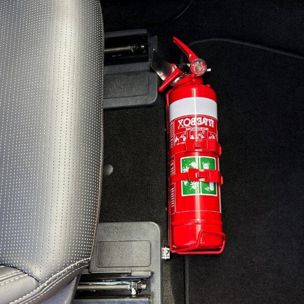 Close-up of a red fire extinguisher held in a KAP bracket at the base of the front seat in a Ford Mustang