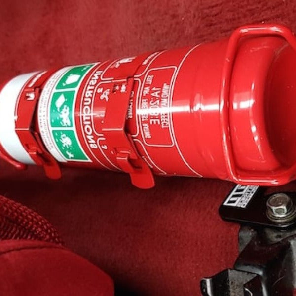 Close-up of a red fire extinguisher held in a KAP bracket at the base of the front seat in a Honda Integra