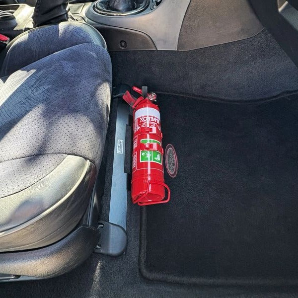 Close-up of a red fire extinguisher held in a KAP bracket at the base of the front seat in a Toyota Echo / Yaris