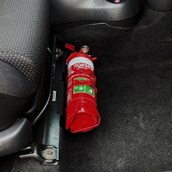 Close-up of a red fire extinguisher held in a KAP bracket at the base of the front seat in a Toyota Echo / Yaris