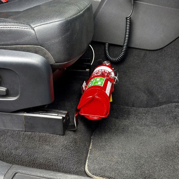 Close-up of a red fire extinguisher held in a KAP bracket at the base of the front seat in a Land Rover Discovery