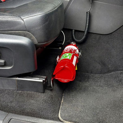 Close-up of a red fire extinguisher held in a KAP bracket at the base of the front seat in a Land Rover Discovery