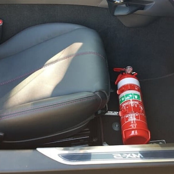 Mazda MX-5 Miata cabin with a red fire extinguisher mounted on a KAP bracket at the base of the left front seat