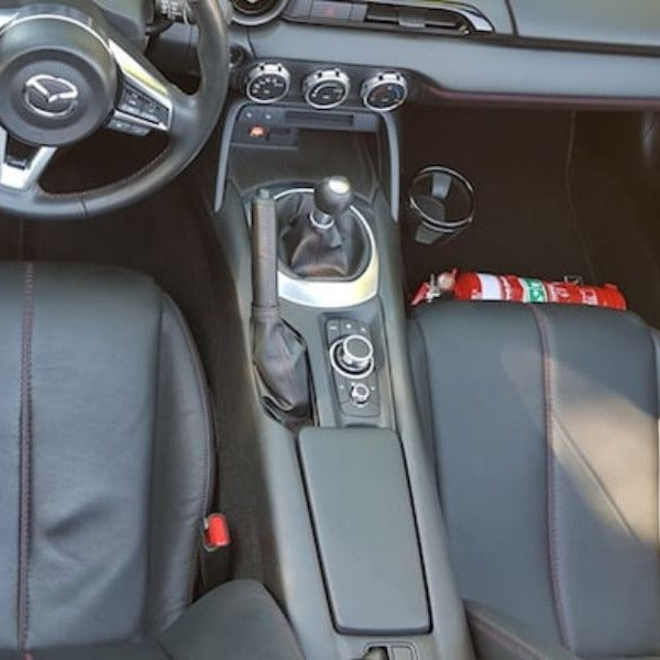 Mazda MX-5 Miata cabin with a red fire extinguisher mounted on a KAP bracket at the base of the left front seat