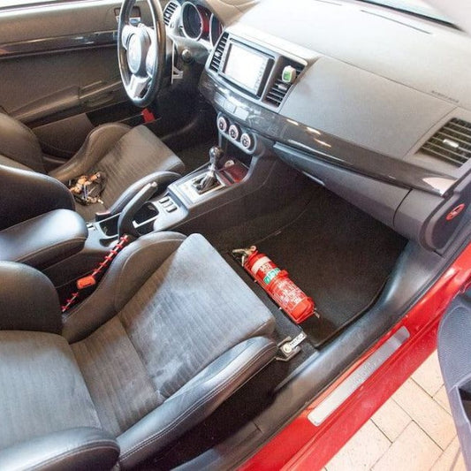 Mitsubishi Lancer Evolution X cabin with a red fire extinguisher mounted on a KAP bracket at the base of the left front seat
