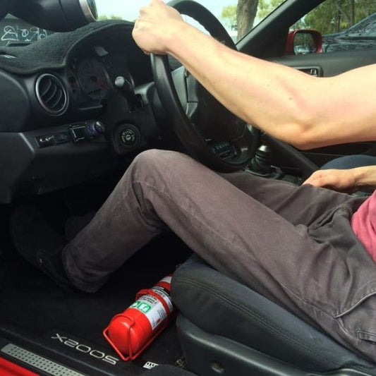 Person seated in a Nissan 240SX, showing the foot room beside the extinguisher at the base of the right front seat