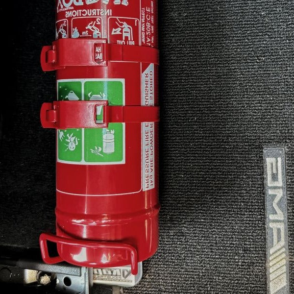 Close-up of a red fire extinguisher held in a KAP bracket at the base of the front seat in a Porsche 718 Boxster