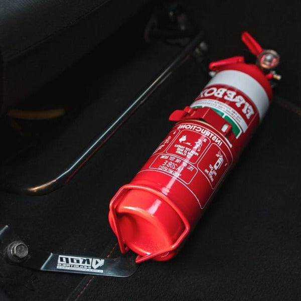 Close-up of a red fire extinguisher held in a KAP bracket at the base of the front seat in a Subaru Levorg