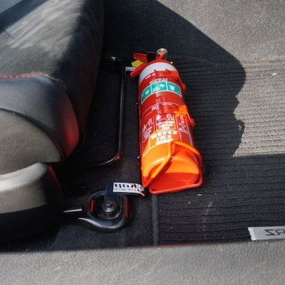 Close-up of a red fire extinguisher held in a KAP bracket at the base of the front seat in a Toyota 86/GT86