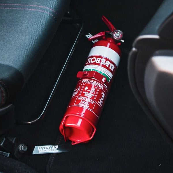 Close-up of a red fire extinguisher held in a KAP bracket at the base of the front seat in a Subaru Impreza WRX / STI