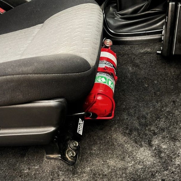 Close-up of a red fire extinguisher held in a KAP bracket at the base of the front seat in a Subaru WRX
