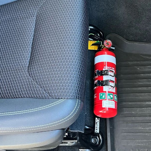 Close-up of a red fire extinguisher held in a KAP bracket at the base of the front seat in a Subaru WRX