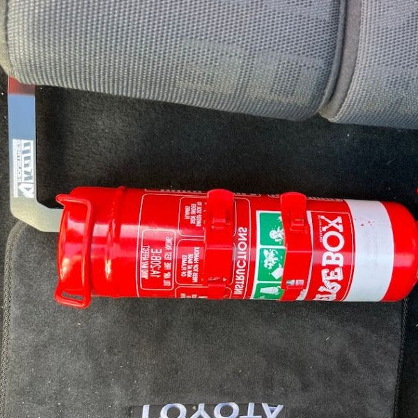Close-up of a red fire extinguisher held in a KAP bracket at the base of the front seat in a Toyota MR2