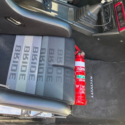 Toyota MR2 cabin with a red fire extinguisher mounted on a KAP bracket at the base of the front seat