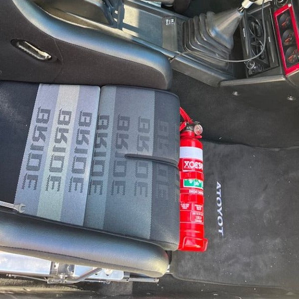 Toyota MR2 cabin with a red fire extinguisher mounted on a KAP bracket at the base of the front seat