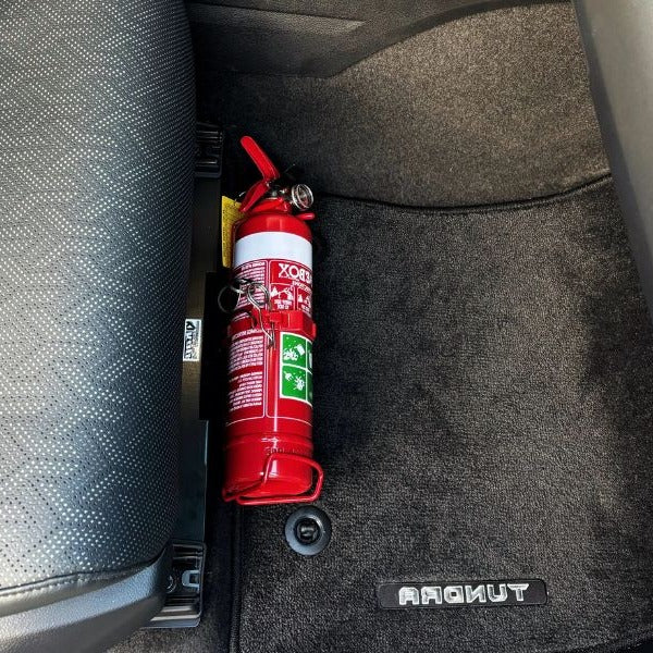 Close-up of a red fire extinguisher held in a KAP bracket at the base of the front seat in a Toyota Land Cruiser