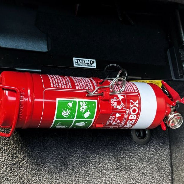 Close-up of a red fire extinguisher held in a KAP bracket at the base of the front seat in a Toyota Land Cruiser