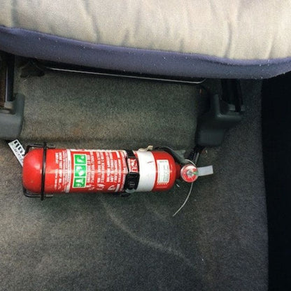 Close-up of a red fire extinguisher held in a KAP bracket at the base of the front seat in a Toyota FJ Cruiser