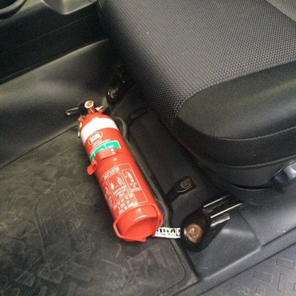 Close-up of a red fire extinguisher held in a KAP bracket at the base of the front seat in a Toyota FJ Cruiser