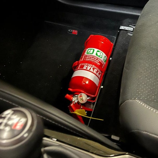 Close-up of a red fire extinguisher held in a KAP bracket at the base of the front seat in a Toyota Camry