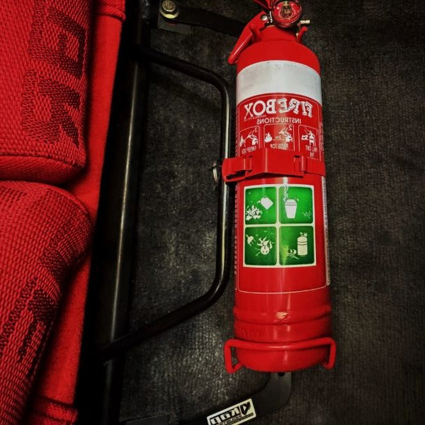 Close-up of a red fire extinguisher held in a KAP bracket at the base of the left front seat in a Toyota Soarer / Lexus SC