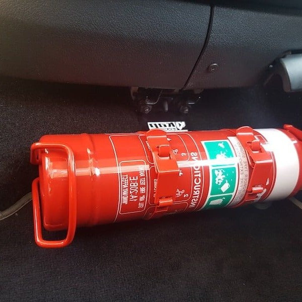 Close-up of a red fire extinguisher held in a KAP bracket at the base of the front seat in a Volkswagen New Beetle