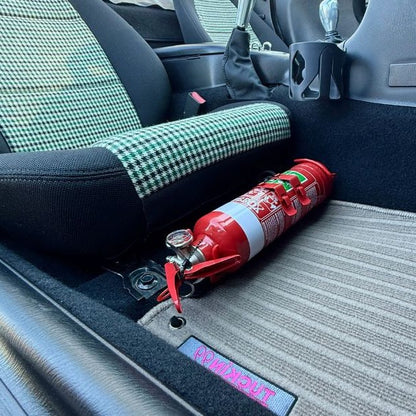 Close-up of a red fire extinguisher held in a KAP bracket at the base of the left front seat in a Mazda MX-5 Miata