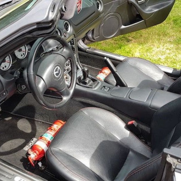 Mazda MX-5 Miata cabin with a red fire extinguisher mounted on a KAP bracket at the base of the left front seat