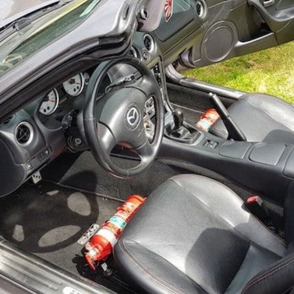Mazda MX-5 Miata cabin with a red fire extinguisher mounted on a KAP bracket at the base of the right front seat