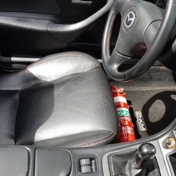 Mazda MX-5 Miata cabin with a red fire extinguisher mounted on a KAP bracket at the base of the right front seat