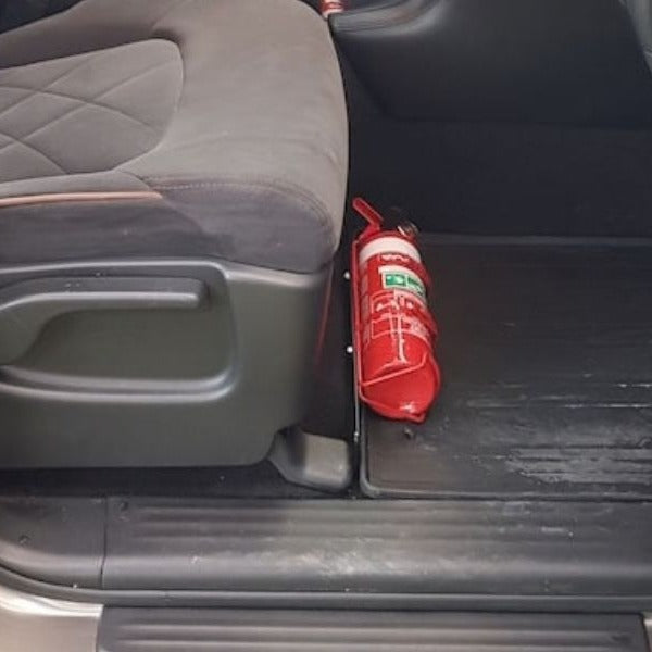 Close-up of a red fire extinguisher held in a KAP bracket at the base of the left front seat in a Nissan Armada