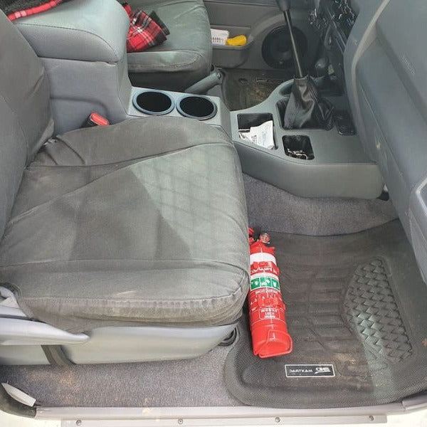 Toyota LandCruiser 80 Series cabin with a red fire extinguisher mounted on a KAP bracket at the base of the left front seat