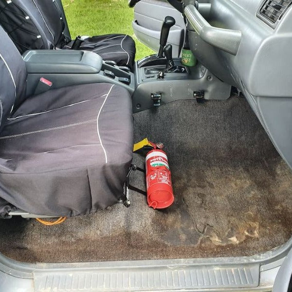 Toyota LandCruiser 80 Series cabin with a red fire extinguisher mounted on a KAP bracket at the base of the left front seat