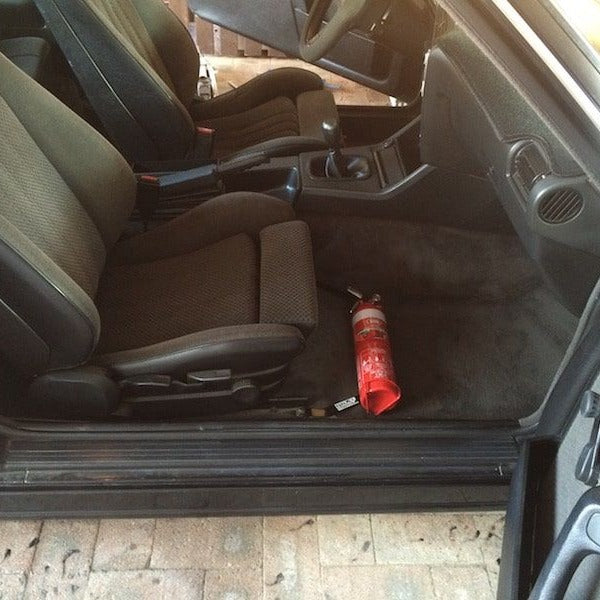 BMW 3 Series cabin with a red fire extinguisher mounted on a KAP bracket at the base of the front seat