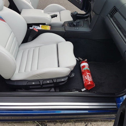 BMW 3 Series cabin with a red fire extinguisher mounted on a KAP bracket at the base of the front seat