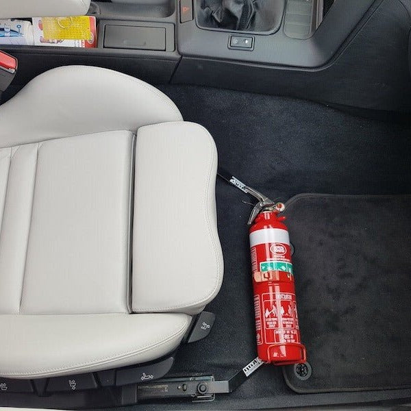 Close-up of a red fire extinguisher held in a KAP bracket at the base of the front seat in a BMW 3 Series
