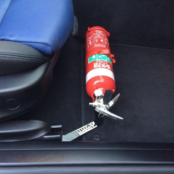 Close-up of a red fire extinguisher held in a KAP bracket at the base of the front seat in a BMW Z4 / Z4 M