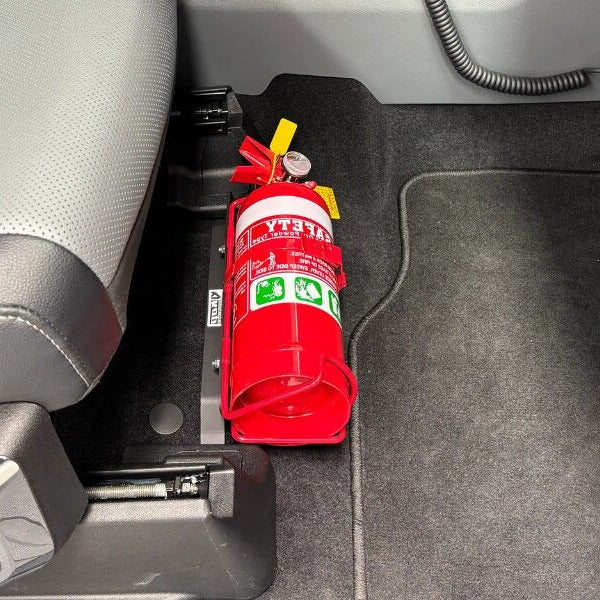 Close-up of a red fire extinguisher held in a KAP bracket at the base of the front seat in a Ford F-150