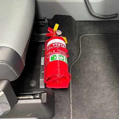 Close-up of a red fire extinguisher held in a KAP bracket at the base of the front seat in a Ford F-150