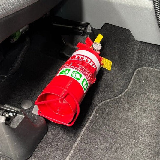 Close-up of a red fire extinguisher held in a KAP bracket at the base of the front seat in a Ford F-150