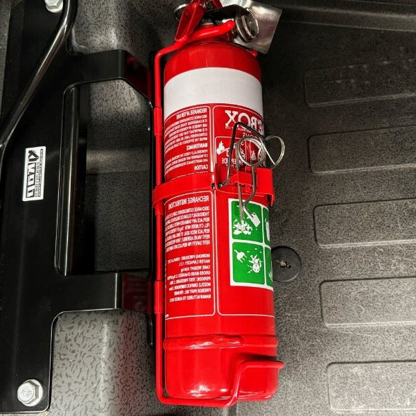 Close-up of a red fire extinguisher held in a KAP bracket at the base of the front seat in a Ineos Quartermaster