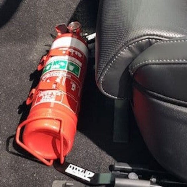 Close-up of a red fire extinguisher held in a KAP bracket at the base of the front seat in a Kia Stinger