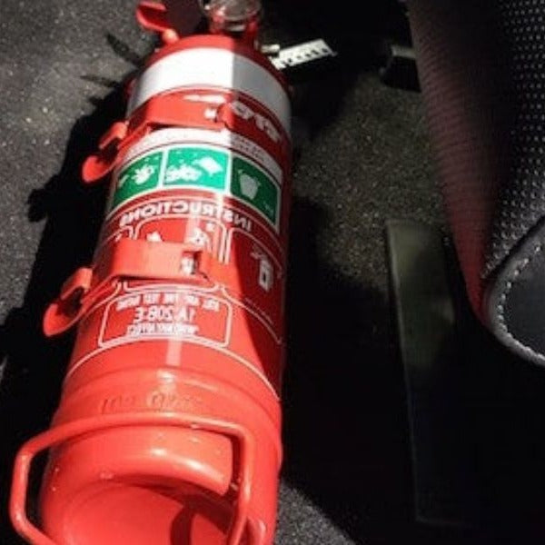 Close-up of a red fire extinguisher held in a KAP bracket at the base of the front seat in a Kia Stinger