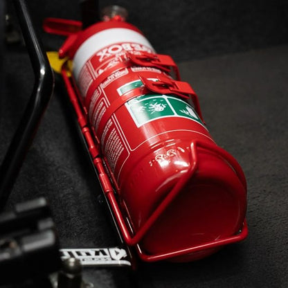 Close-up of a red fire extinguisher held in a KAP bracket at the base of the left front seat in a Mitsubishi Evo VIII